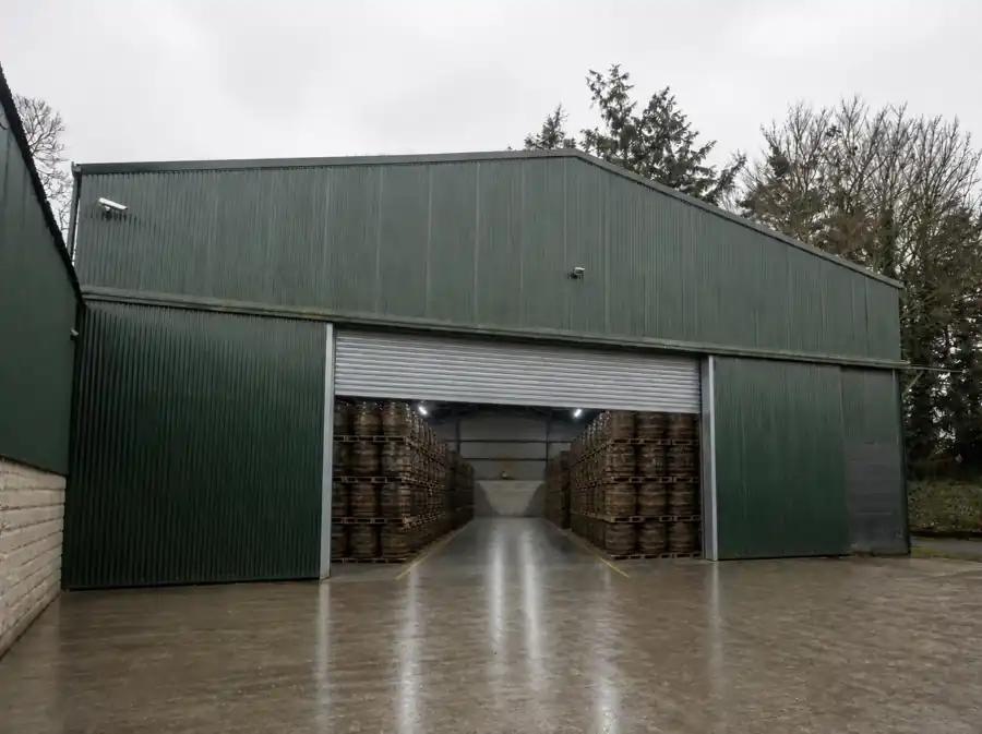 Concept view of Unit 2, a green-clad warehouse with its roller door open onto palletised casks
